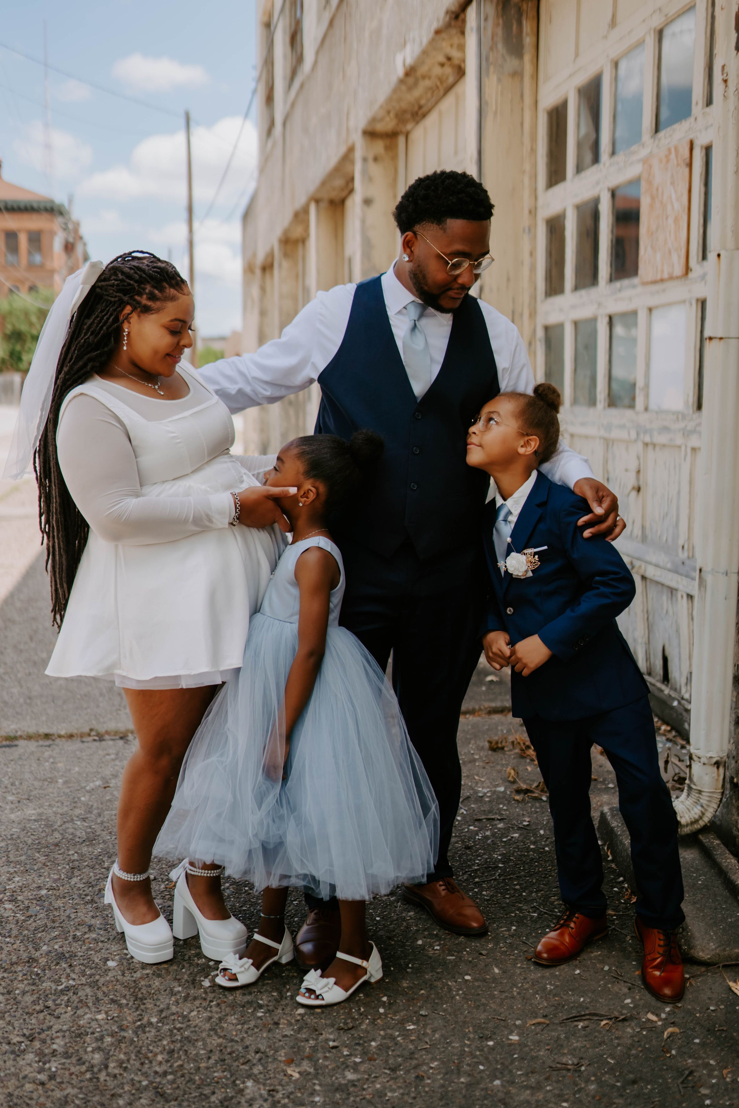A family shares playful moments together in formal attire against an architectural backdrop.