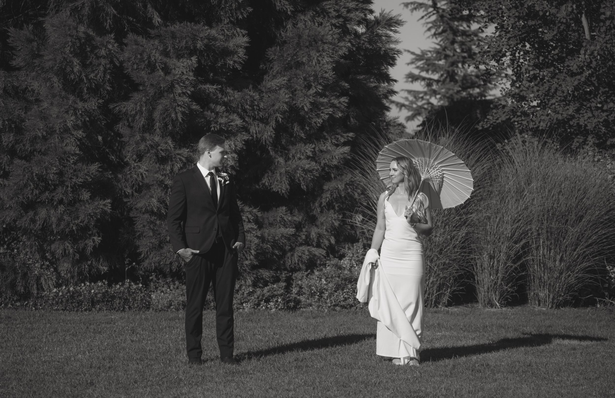 A vintage black and white photograph showing a couple in formal attire standing in a garden setting.
