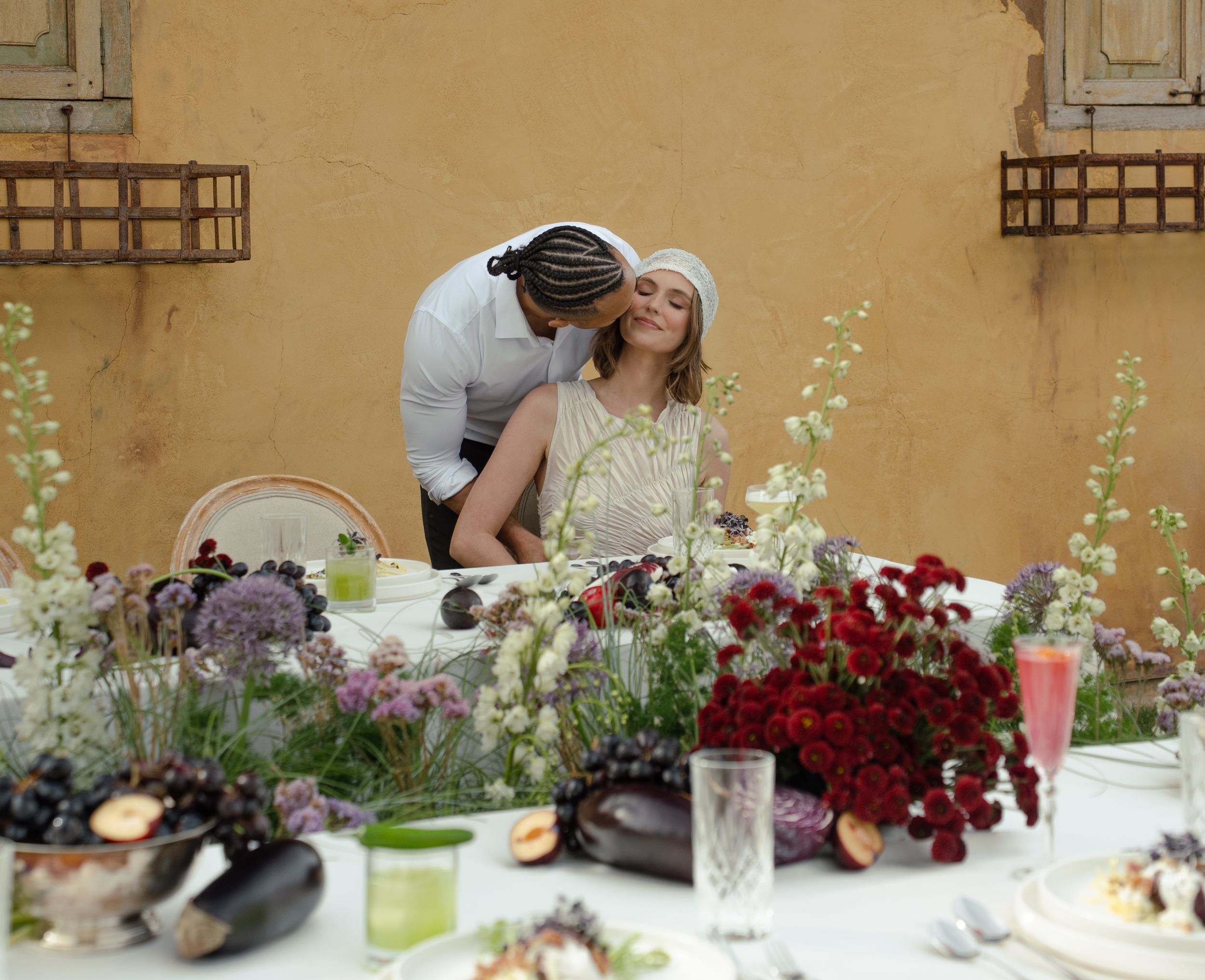 Couple sharing a romantic moment at an elegantly decorated outdoor dining table with lush floral arrangements.
