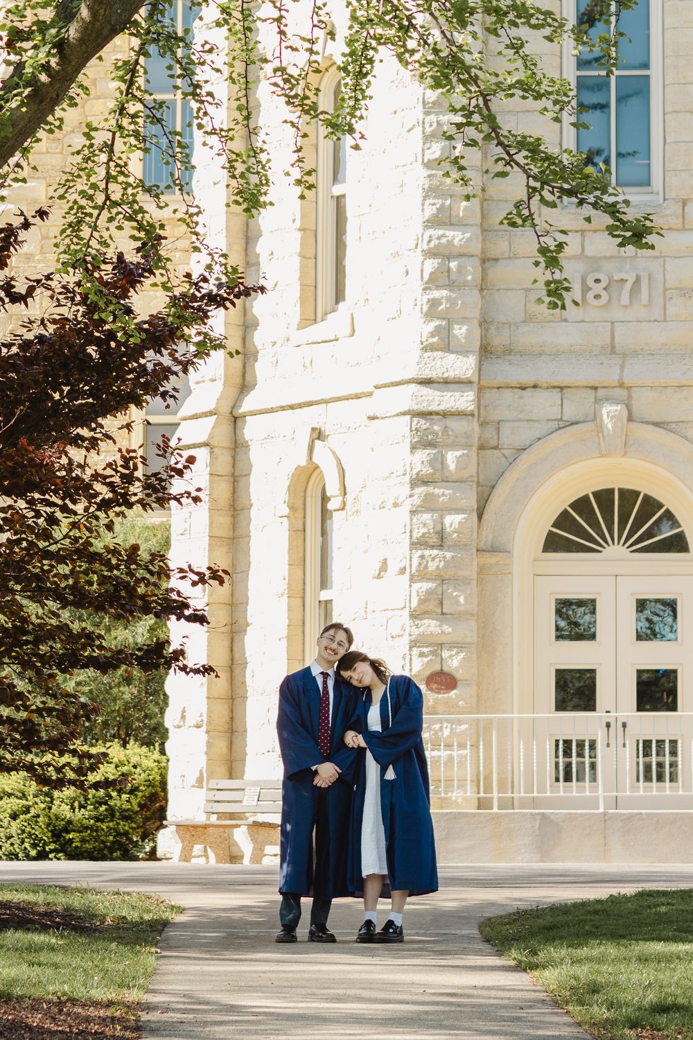 Two people in navy suits share a special sunrise moment on the grounds of an elegant limestone building with classic architecture.