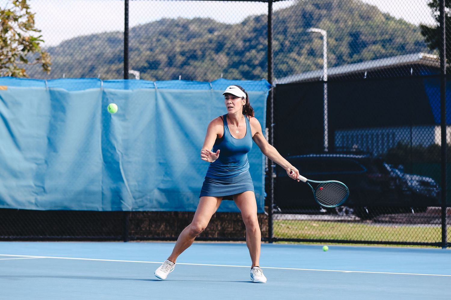 Tennis player preparing to hit a backhand shot on a court with Cairns Council branding visible in the background.