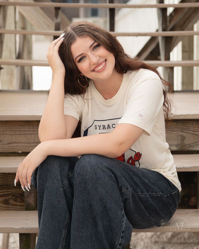 A casual portrait on wooden stairs features a white t-shirt and jeans outfit.