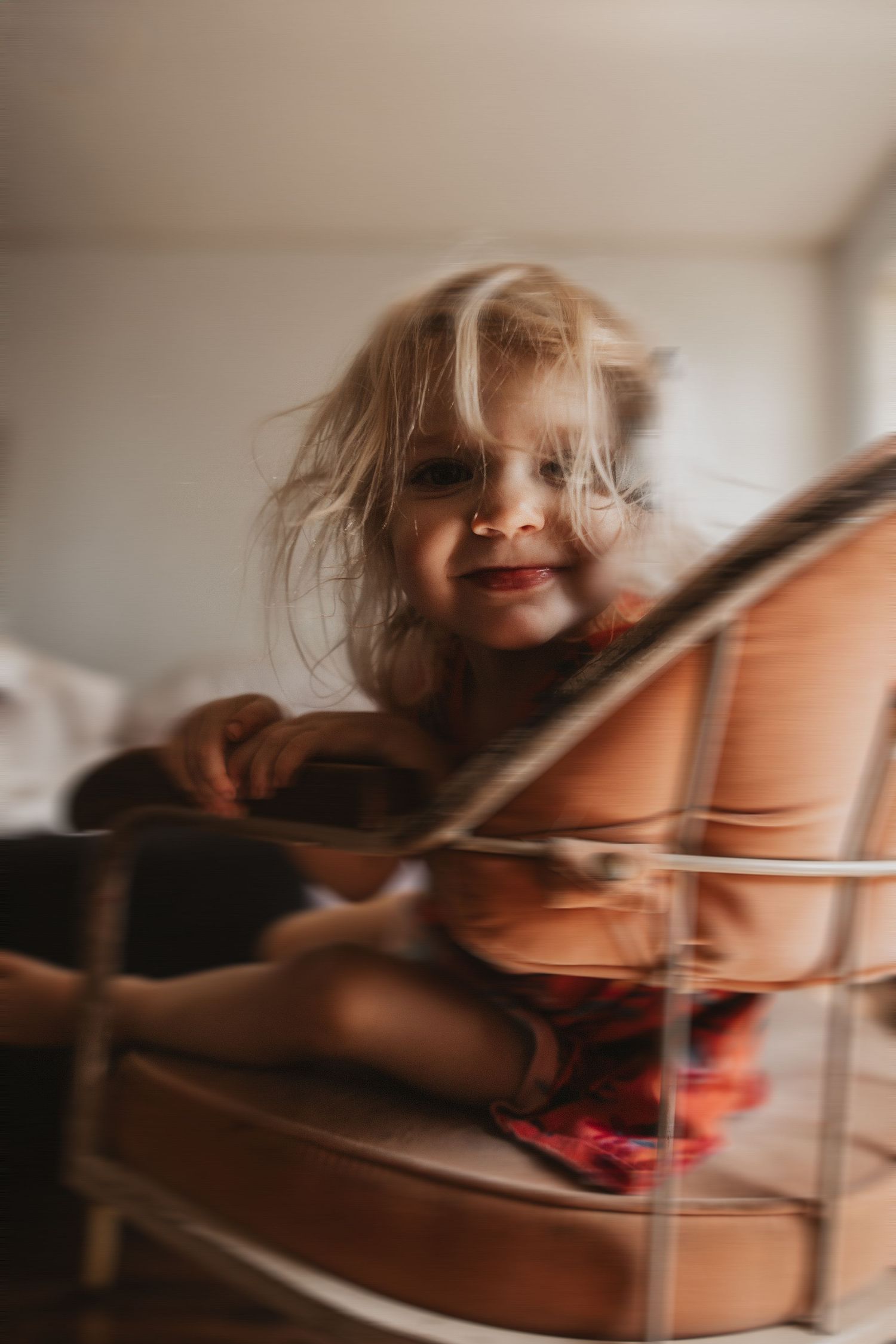 Close-up shot of a young child with blonde hair spinning in a vintage office chair in soft, warm lighting.