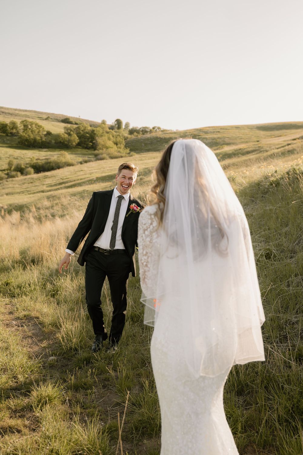 A candid wedding photo of a couple standing in a scenic field with rolling hills in the background.
