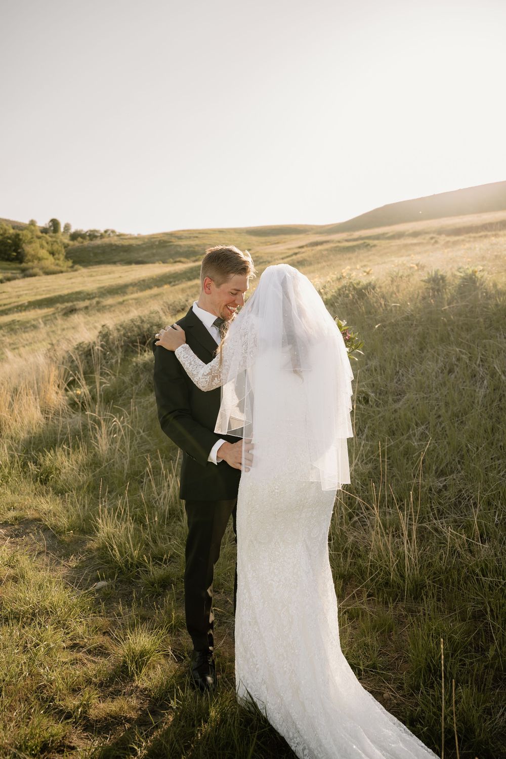 A bride and groom share an intimate moment on a hillside during golden hour.