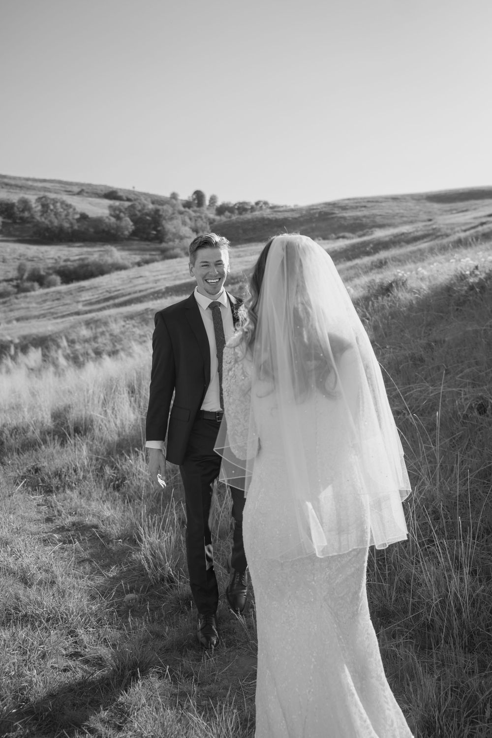 Black and white portrait of newlyweds standing on a grassy hillside path.