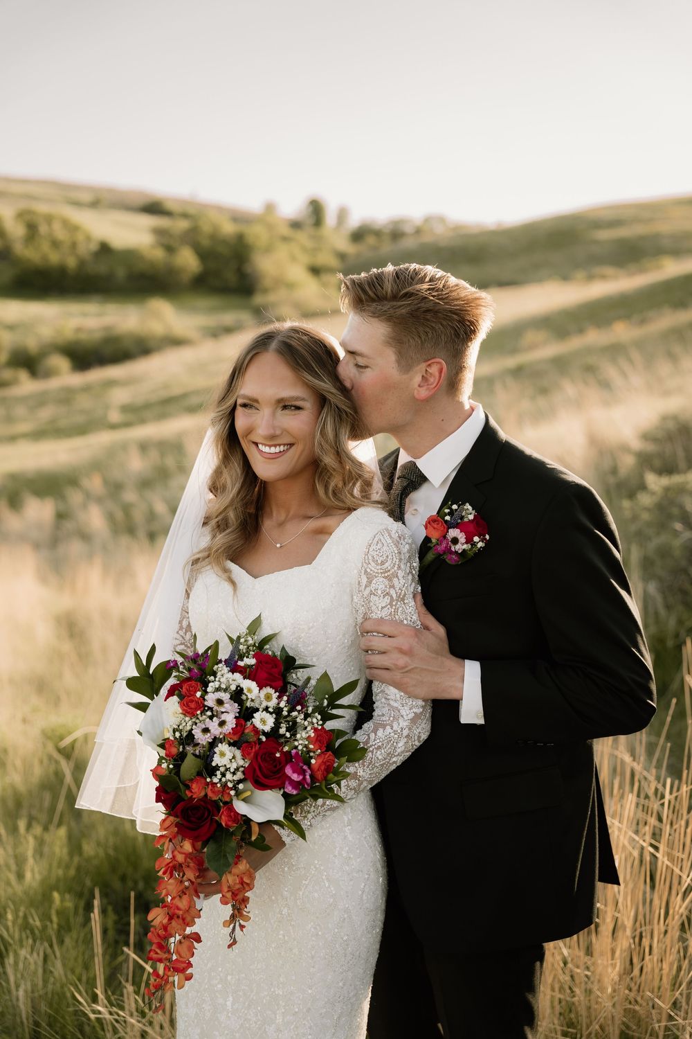 Romantic wedding portrait featuring a beautiful bouquet of red flowers against a sunset mountain landscape.