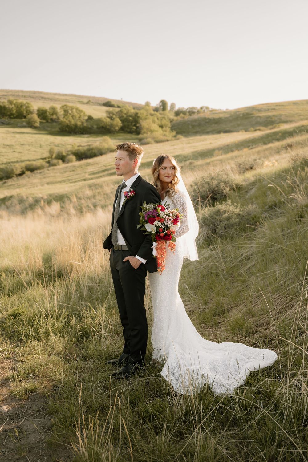 Wedding couple poses back-to-back on golden hill during sunset portrait session.