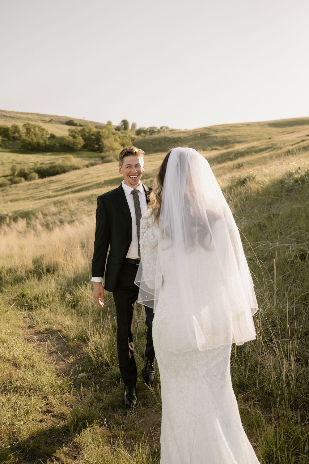 A wedding couple poses on a hillside during golden hour with the bride in a white dress and veil.