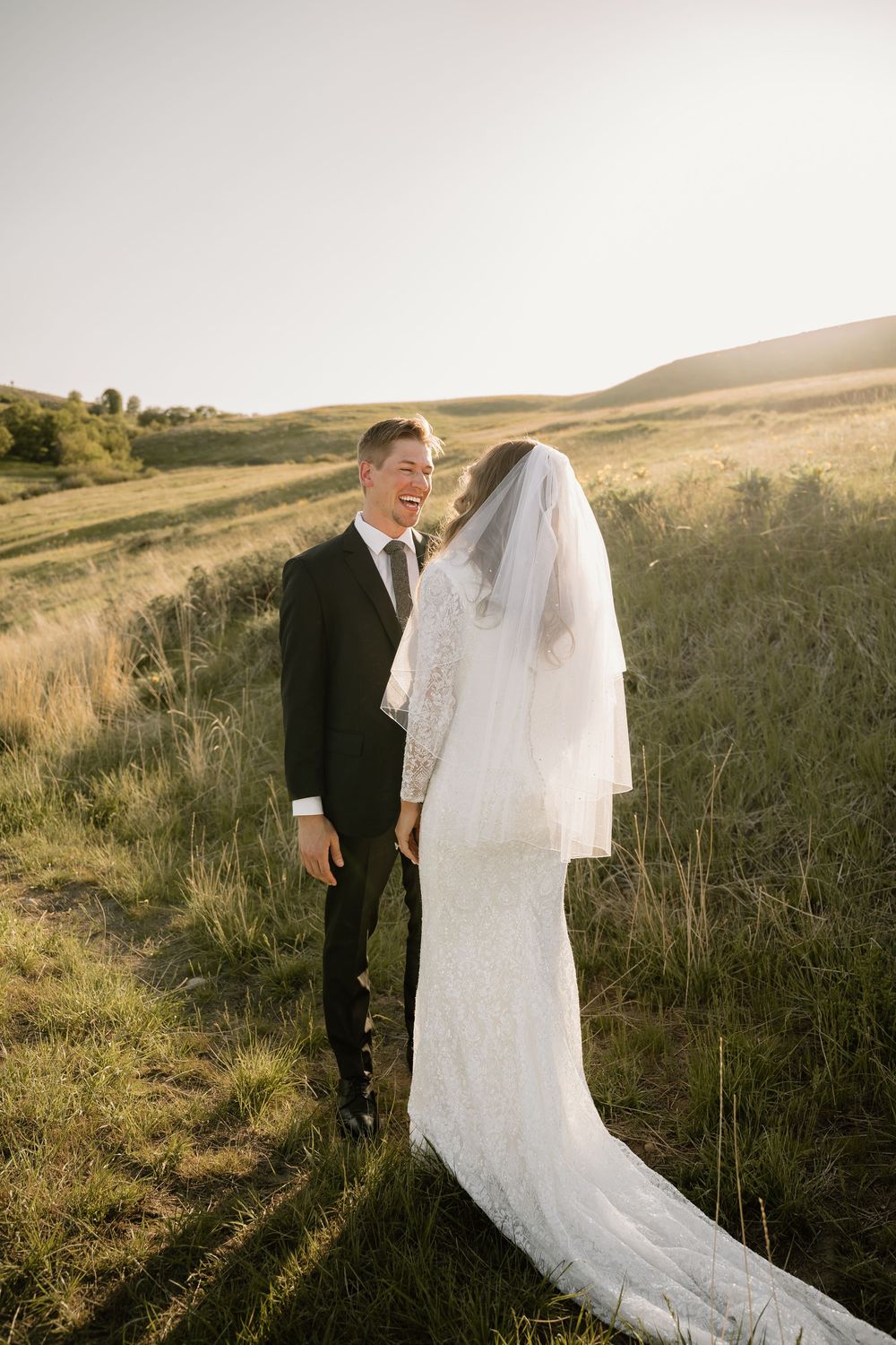 A couple shares an intimate moment in their wedding attire against a backdrop of rolling hills at sunset.