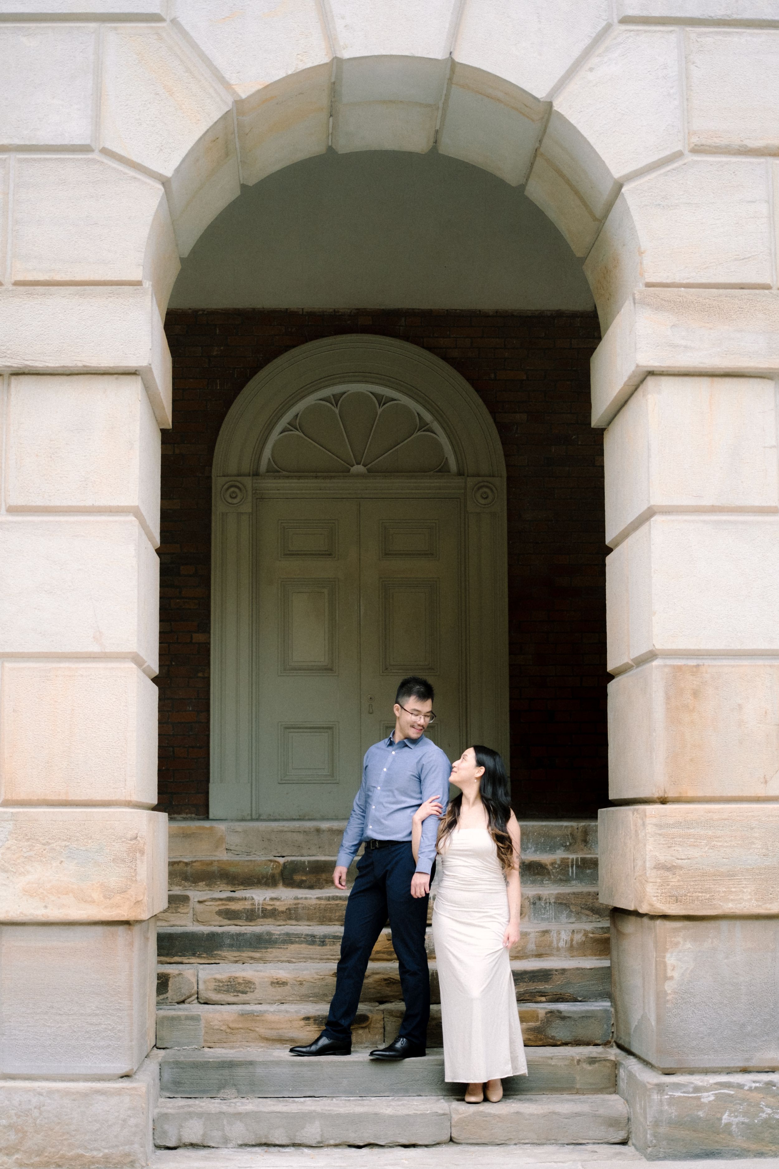 Couple standing on stone steps under arched doorway for engagement photos.