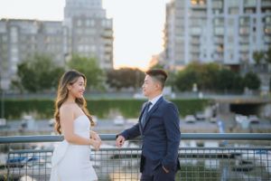Couple in formal attire sharing romantic moment on urban waterfront.