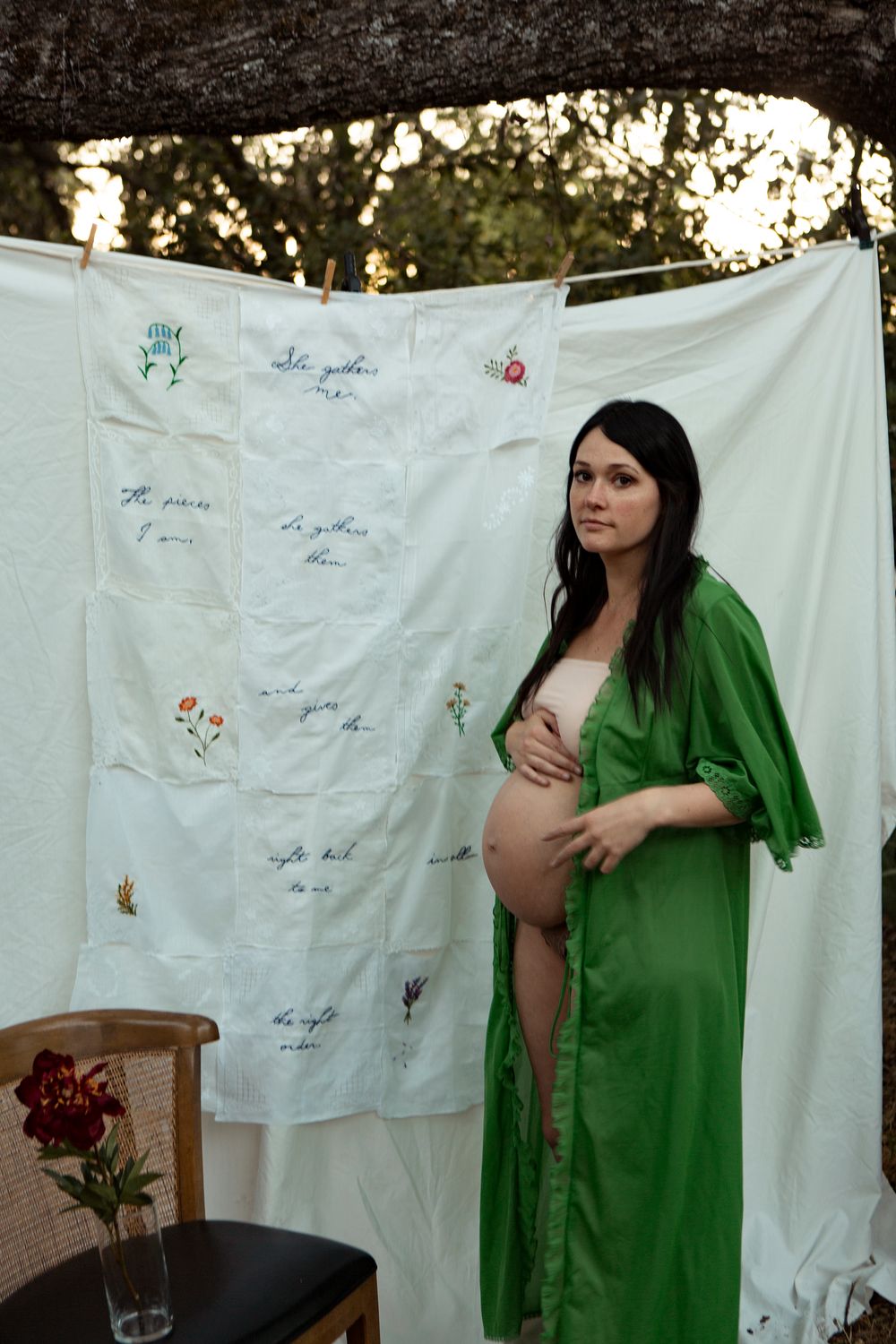 An expectant figure in a green robe poses against a decorated white backdrop with handwritten messages.