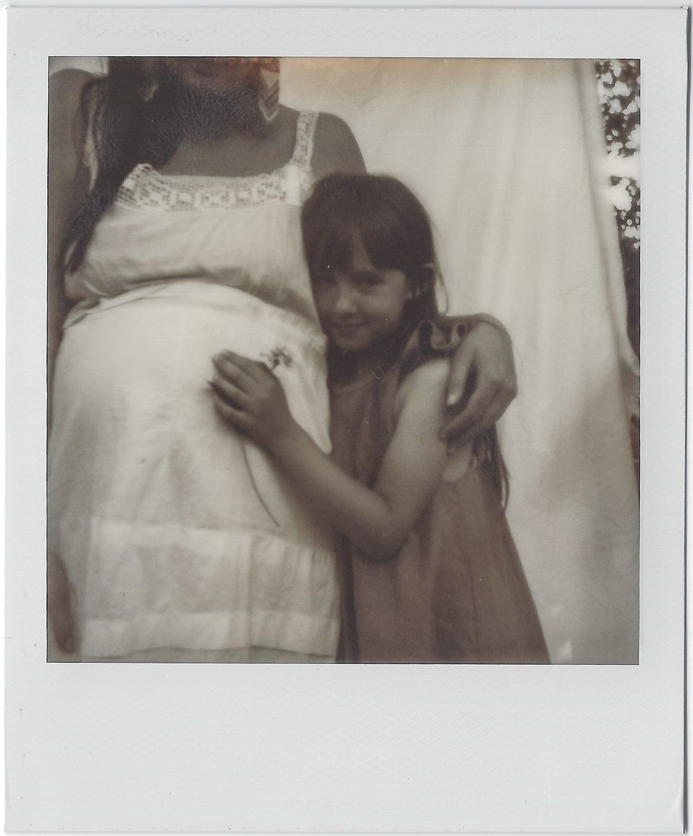 Intimate vintage polaroid showing tender embrace between two people in white clothing.