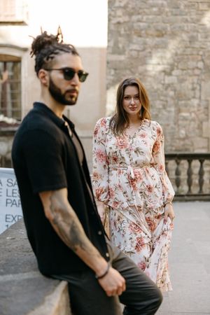Couple in casual attire posing against stone walls in an urban setting.