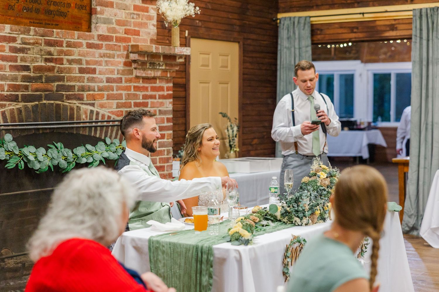 A wedding reception gathering at a rustic brick venue with guests seated at tables during dinner toasts.