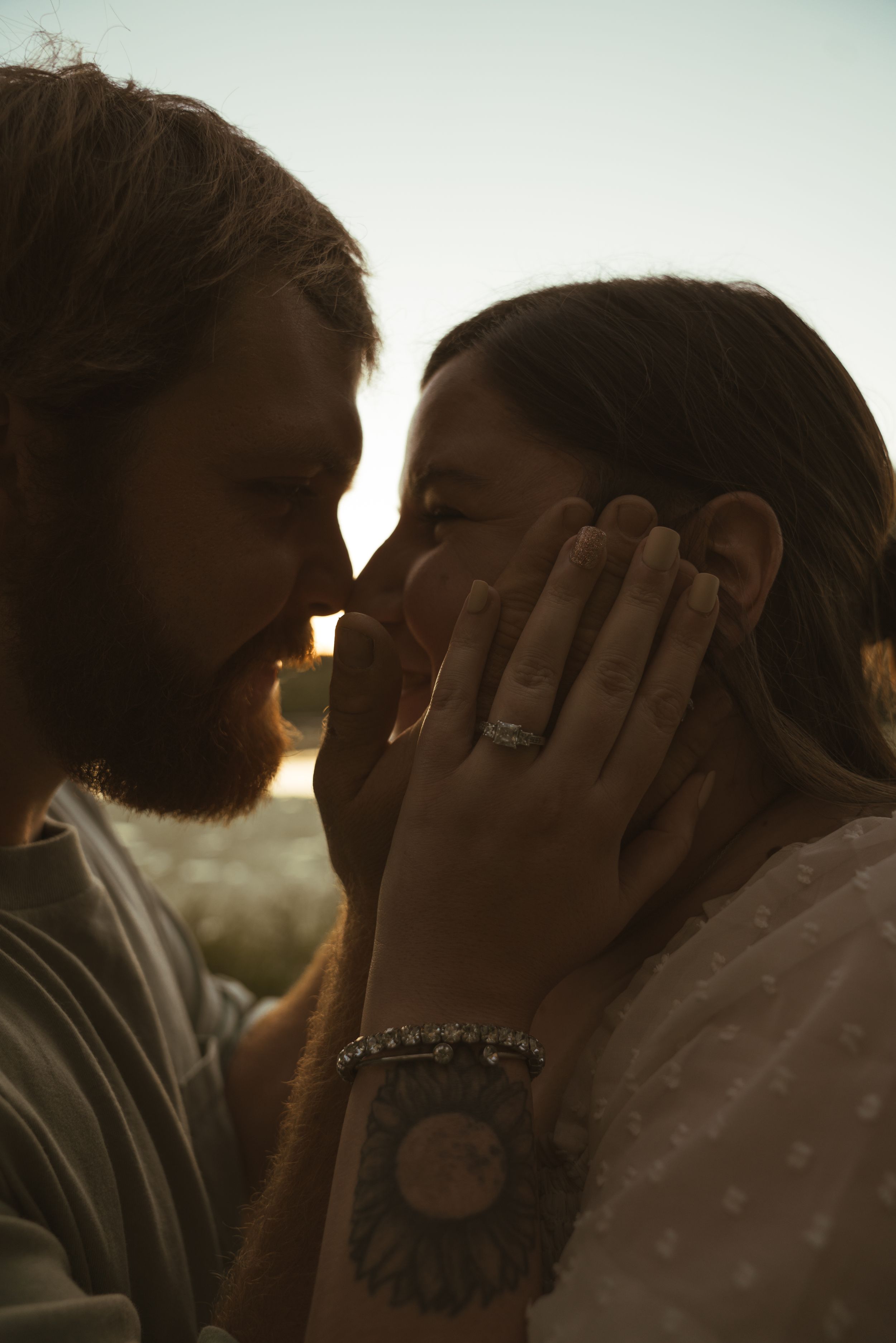 A romantic sunset moment between a couple with hands tenderly touching faces.