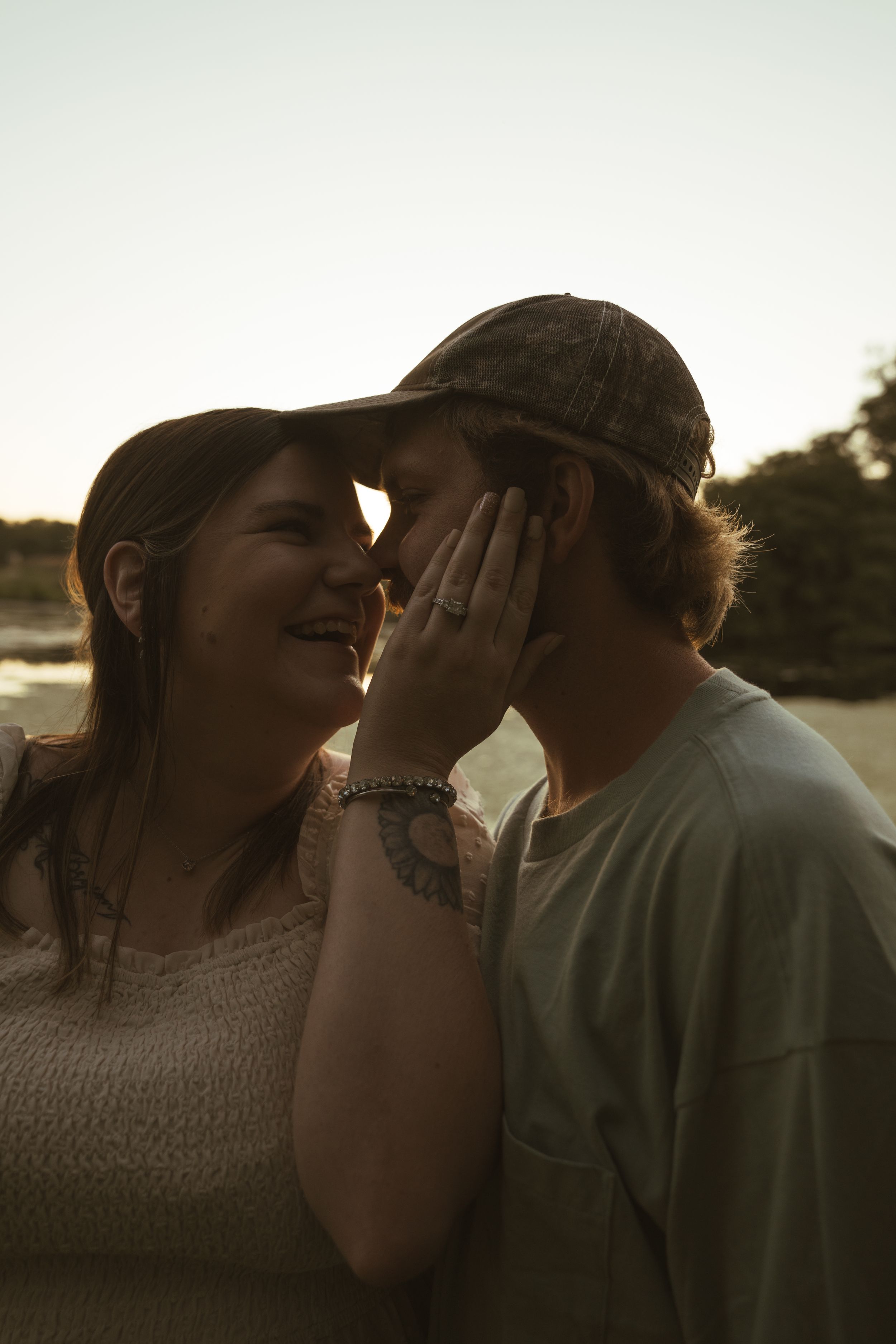 A candid moment between a couple laughing and touching faces at sunset.
