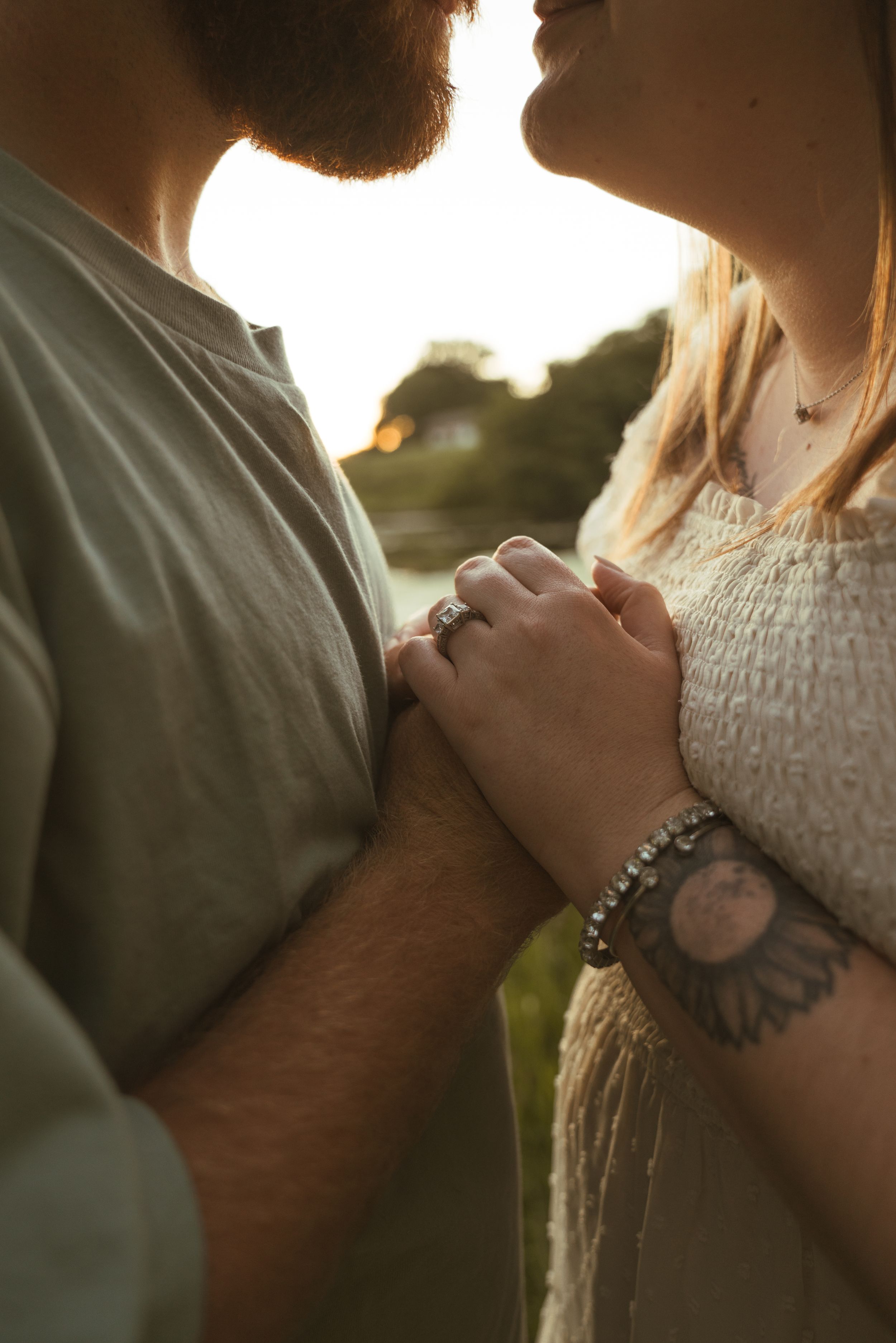 Close-up of couple's hands clasped together with sunlight behind them.