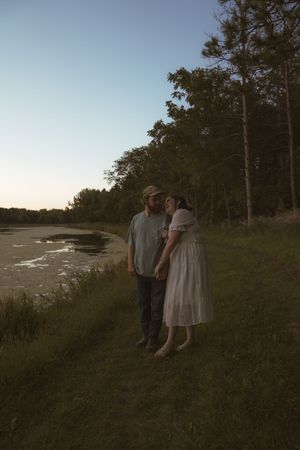 Couple standing together on a grassy hill overlooking a waterfront at dusk.