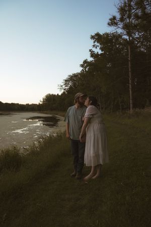 Two people standing on a coastal hillside during sunset with water and trees in the background.