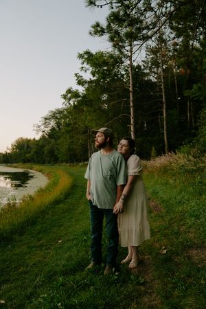 Couple enjoying a peaceful moment together on a grassy path beside a waterway at sunset.