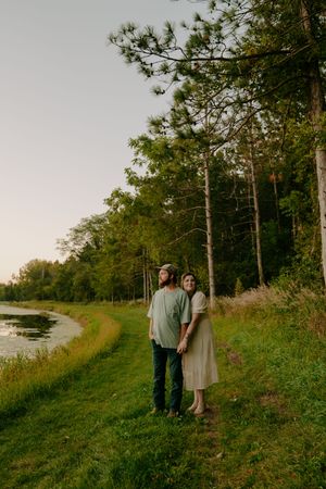 Couple standing together on a green path overlooking water during golden hour.