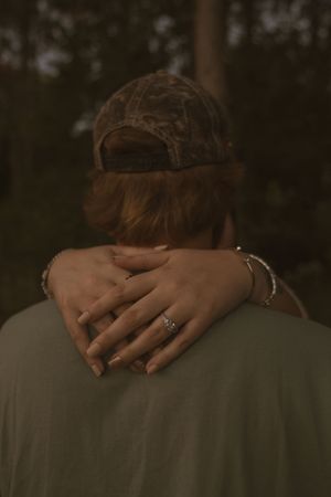 Close-up view of hands embracing on a shoulder in dim evening light.