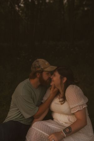 A romantic couple shares an intimate moment in a dark wooded setting, with the woman wearing a white dress.