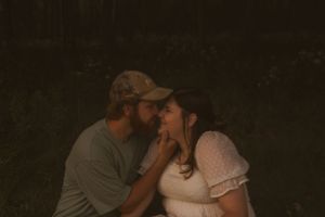 A couple shares a sweet moment together in moody lighting against a dark background.