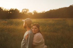 A couple poses together in a golden sunlit field during sunset.