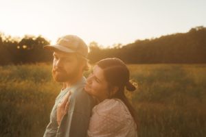 A tender moment between a couple backlit by golden hour sun in a rural field.
