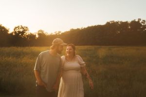 A couple shares a laugh together in a sun-drenched field at golden hour.