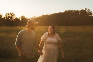 A couple stands together in a golden field during sunset while sharing a moment.