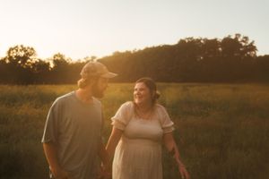 A couple shares a joyful moment in a sunlit field during golden hour.