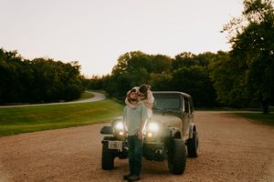 A couple embraces in front of an illuminated off-road vehicle on a dirt path.