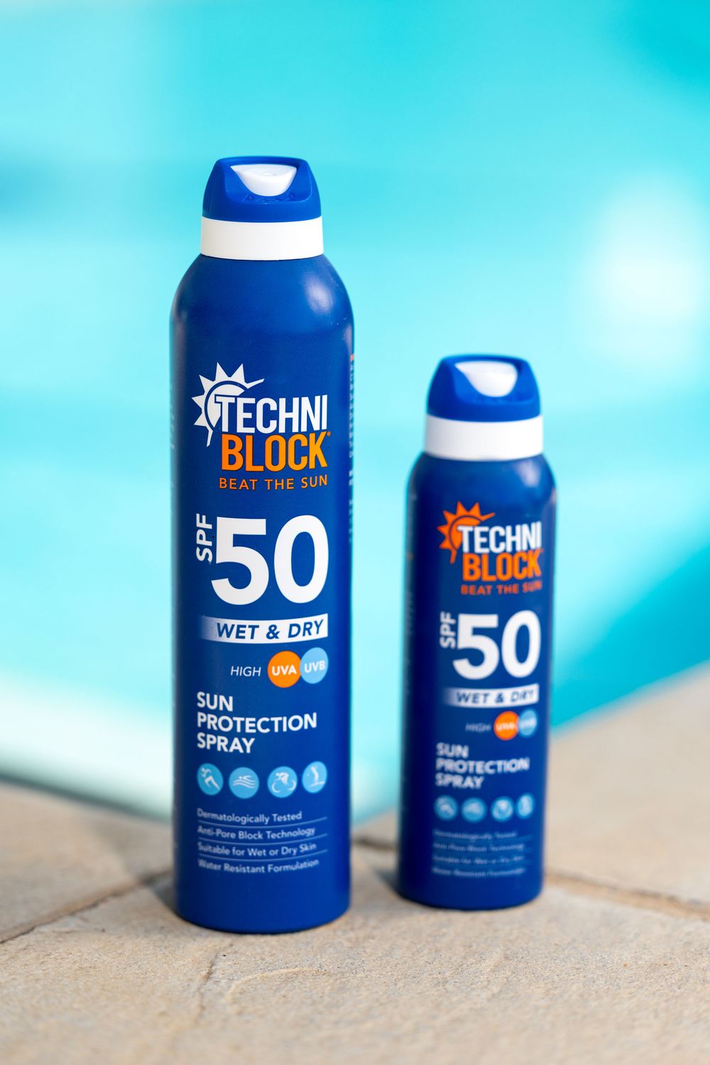 Two Techniblock SPF 50 Wet & Dry Sun Protection Spray bottles by a pool, in large and travel sizes.