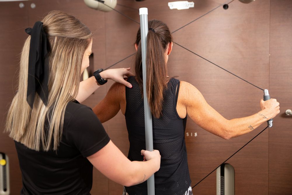 Two people in black workout attire exercising at a cable machine in a fitness facility.