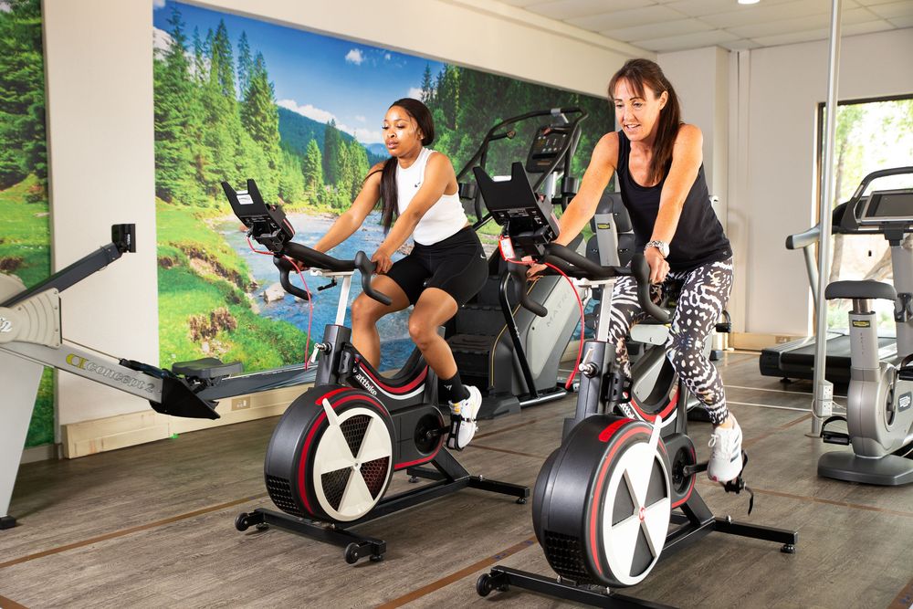 Two people doing cardio workout on spinning bikes in a home gym with a nature backdrop wall mural.