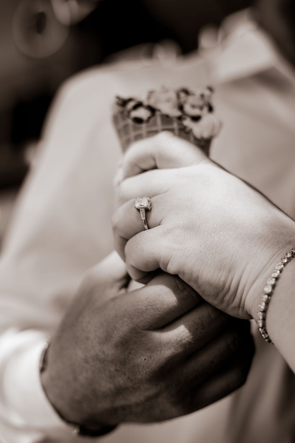 Black and white photo of couple holding ice cream cone, woman wearing diamond engagement ring and pearl bracelet.