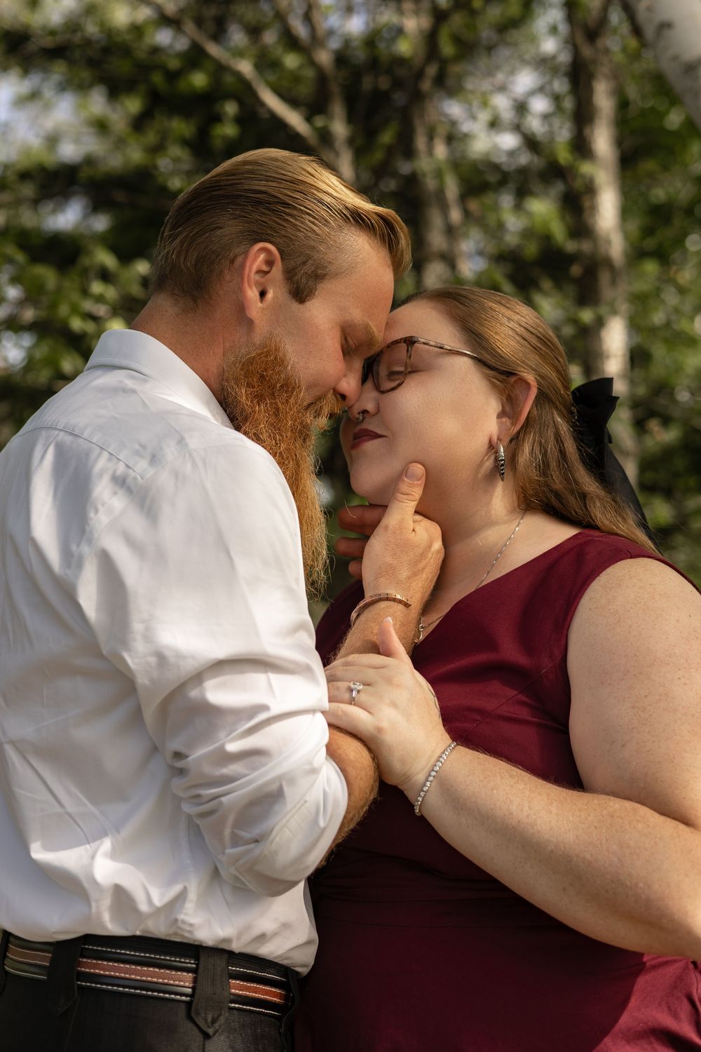 A romantic couple in formal attire share an intimate moment outdoors, with the man tenderly holding the womans chin.