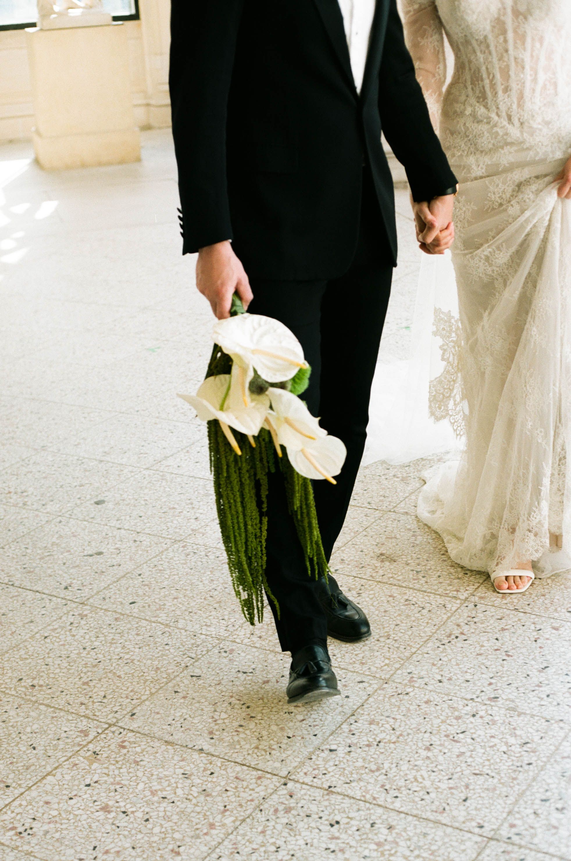 Close-up details of bride and groom's formal attire as they walk together on a terrazzo floor.
