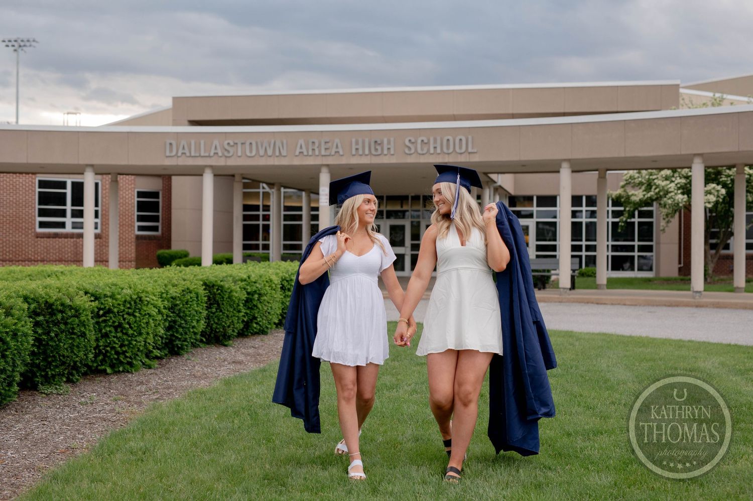 People walking outside a brick building in graduation gowns and summer dresses during a photo shoot.