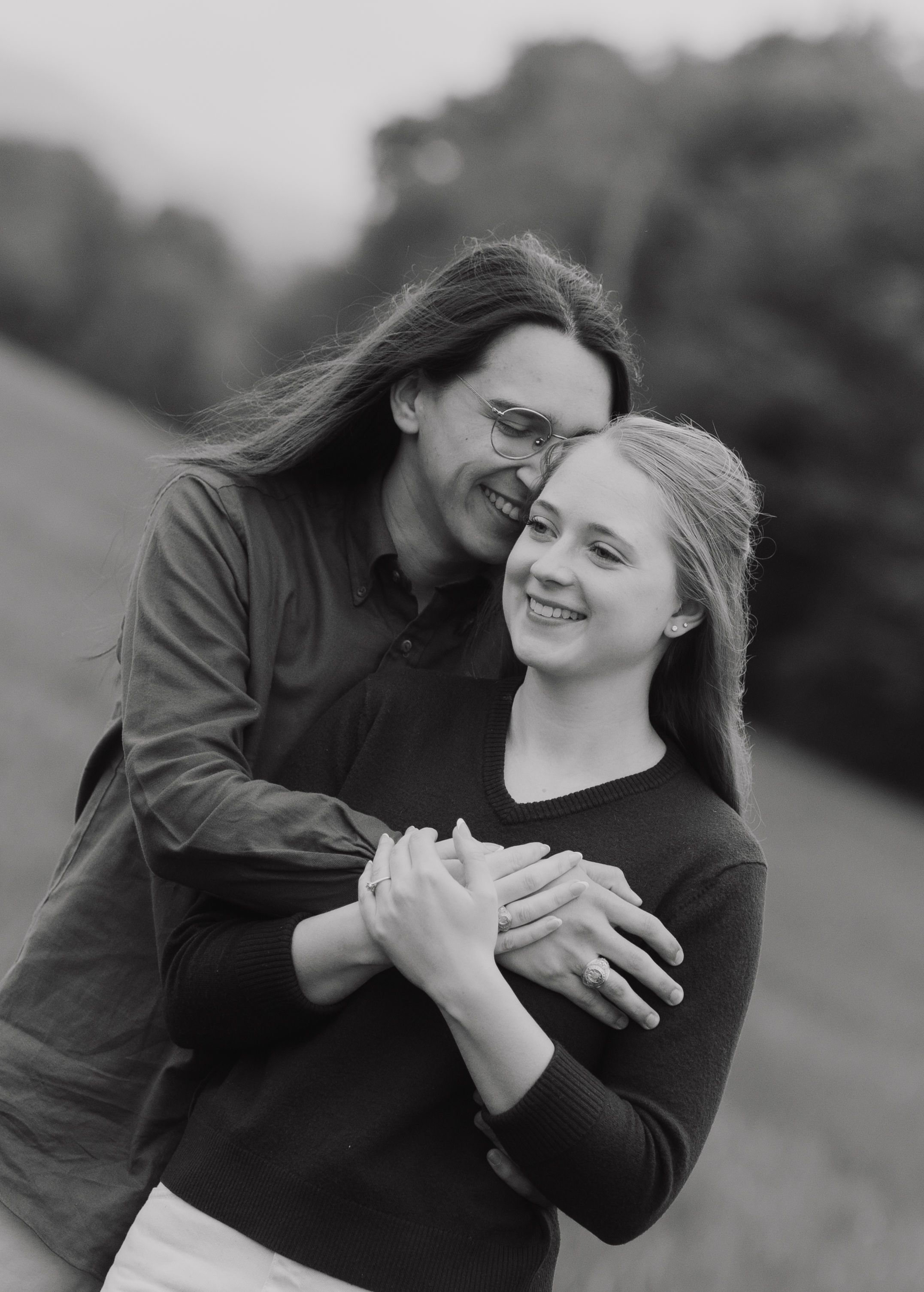 Black and white photo of affectionate couple embracing and smiling while sharing an intimate outdoor moment together.