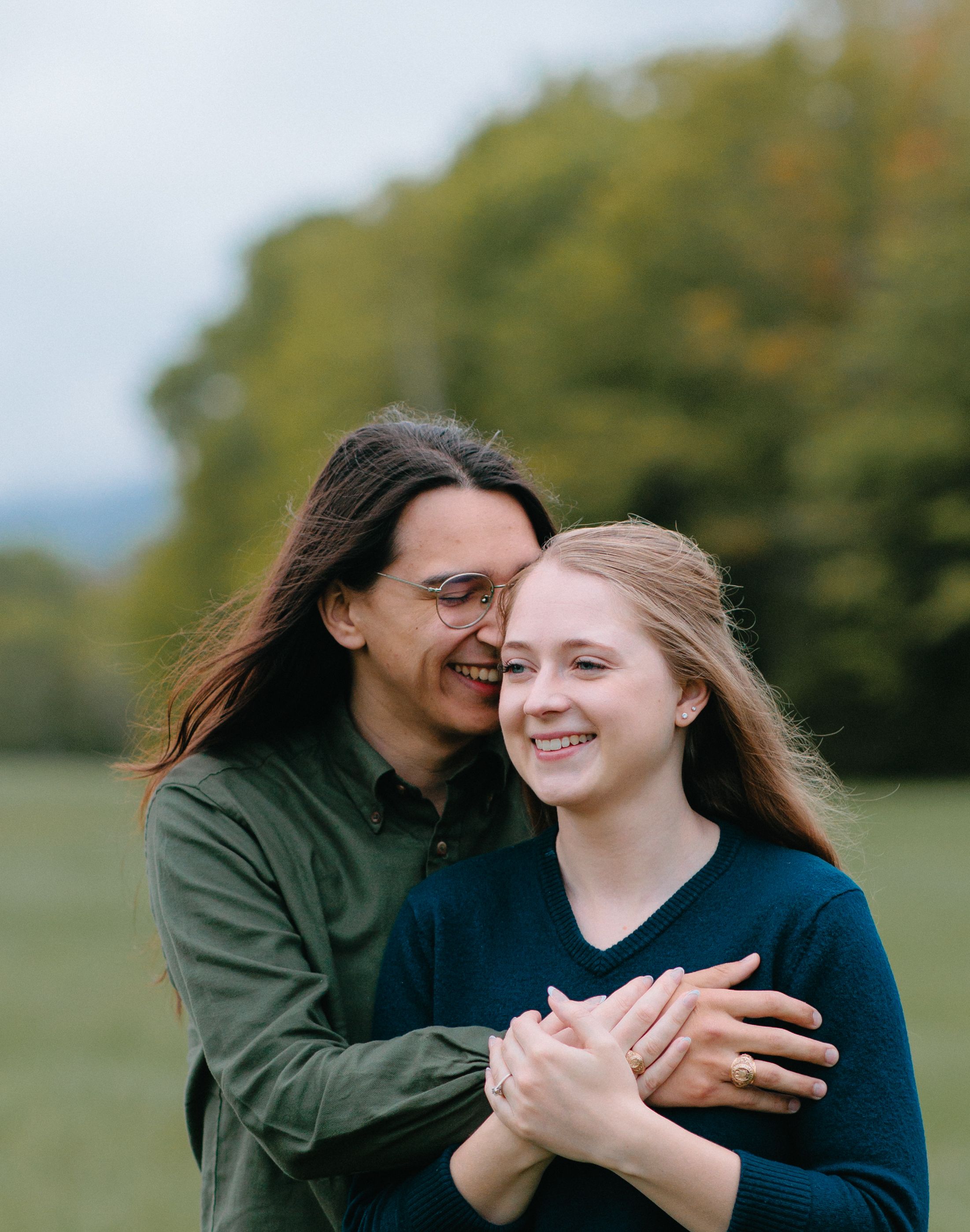 A couple sharing a tender moment together outdoors with autumn trees in the background.
