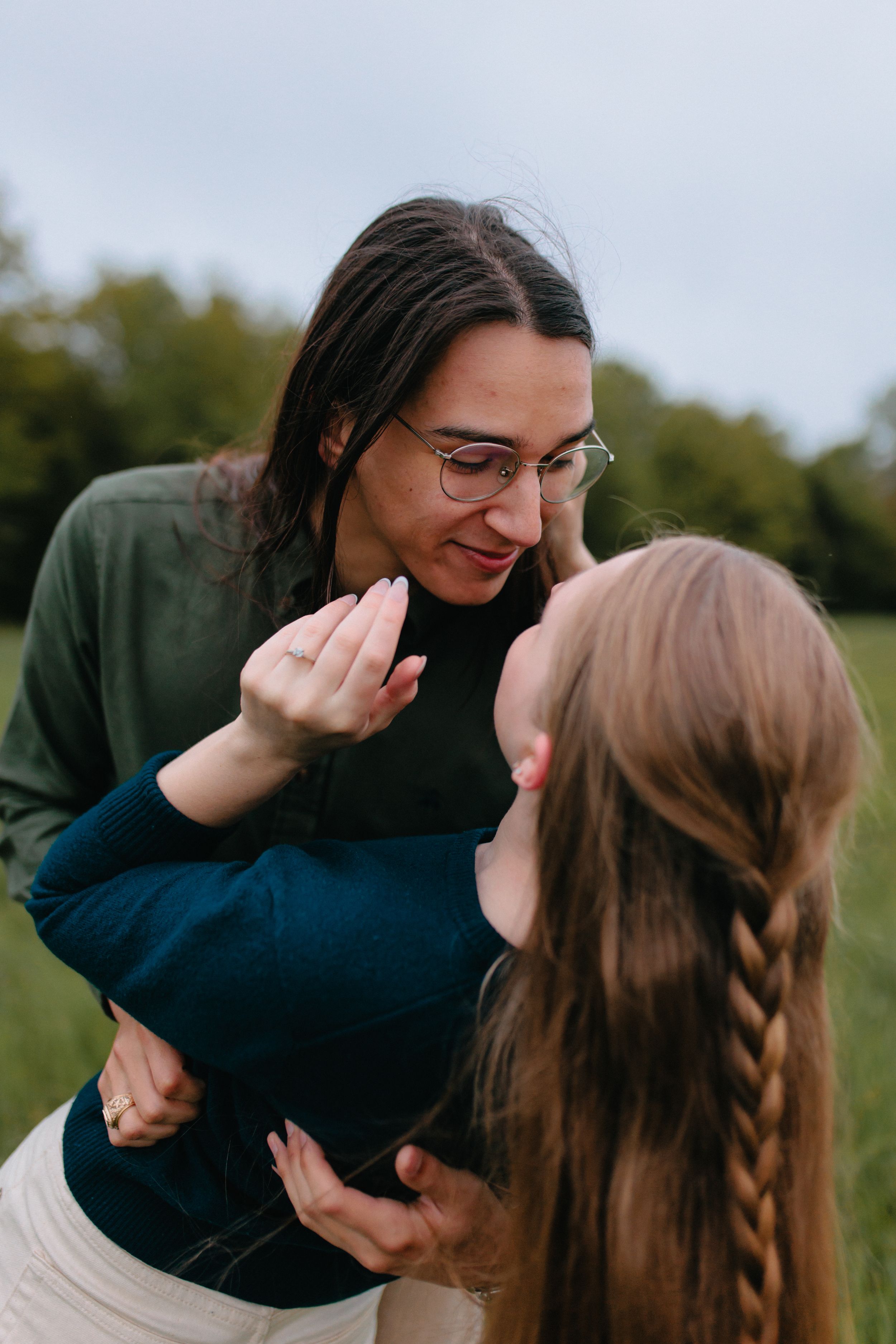 Two people share an intimate laugh while embracing in an outdoor field setting.