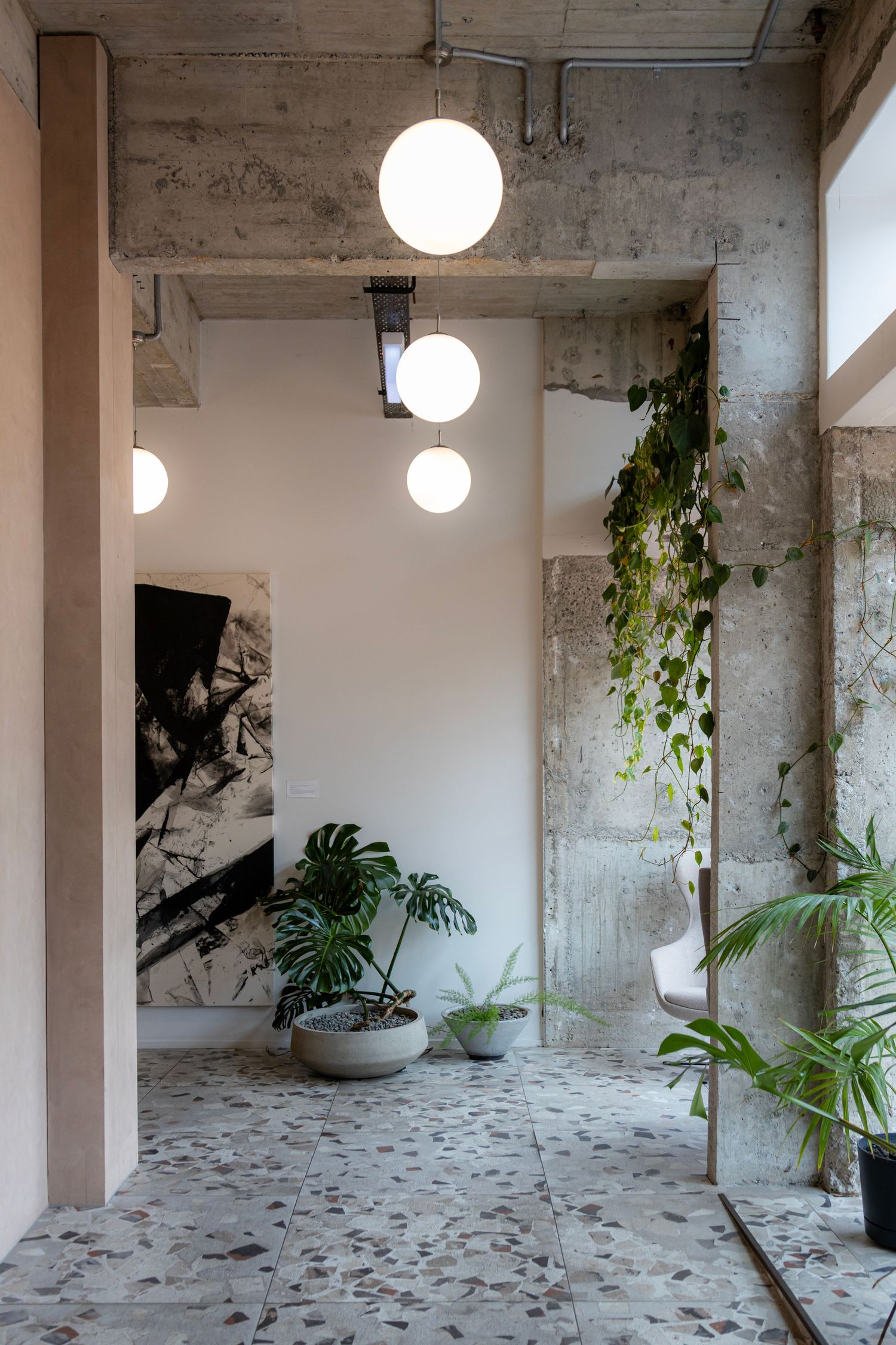 Indoor corridor with terrazzo floors, leafy plants and spherical pendant lights creating a calm, urban oasis.