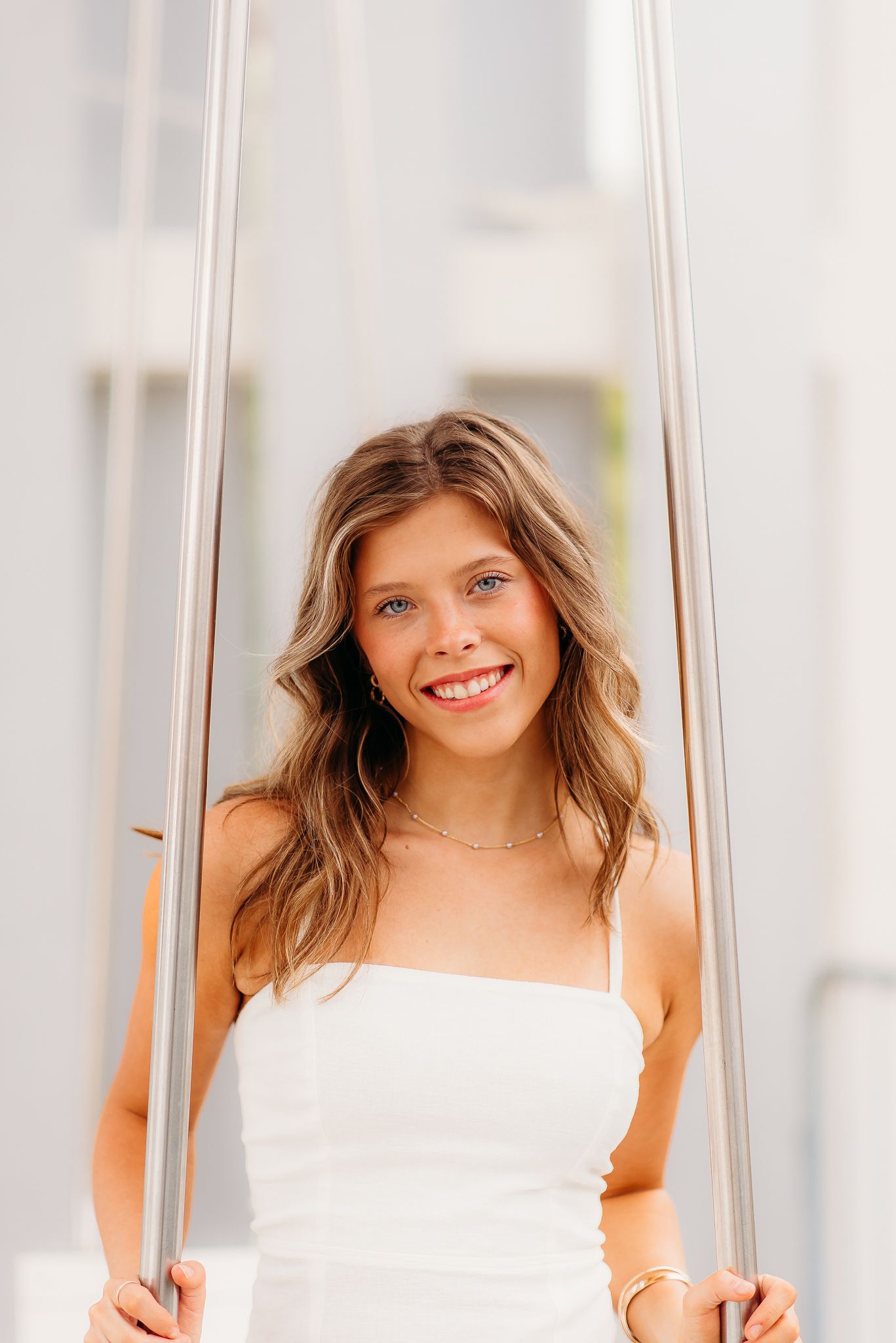 Woman in white strapless dress standing by glass door panels with natural lighting and soft smile.