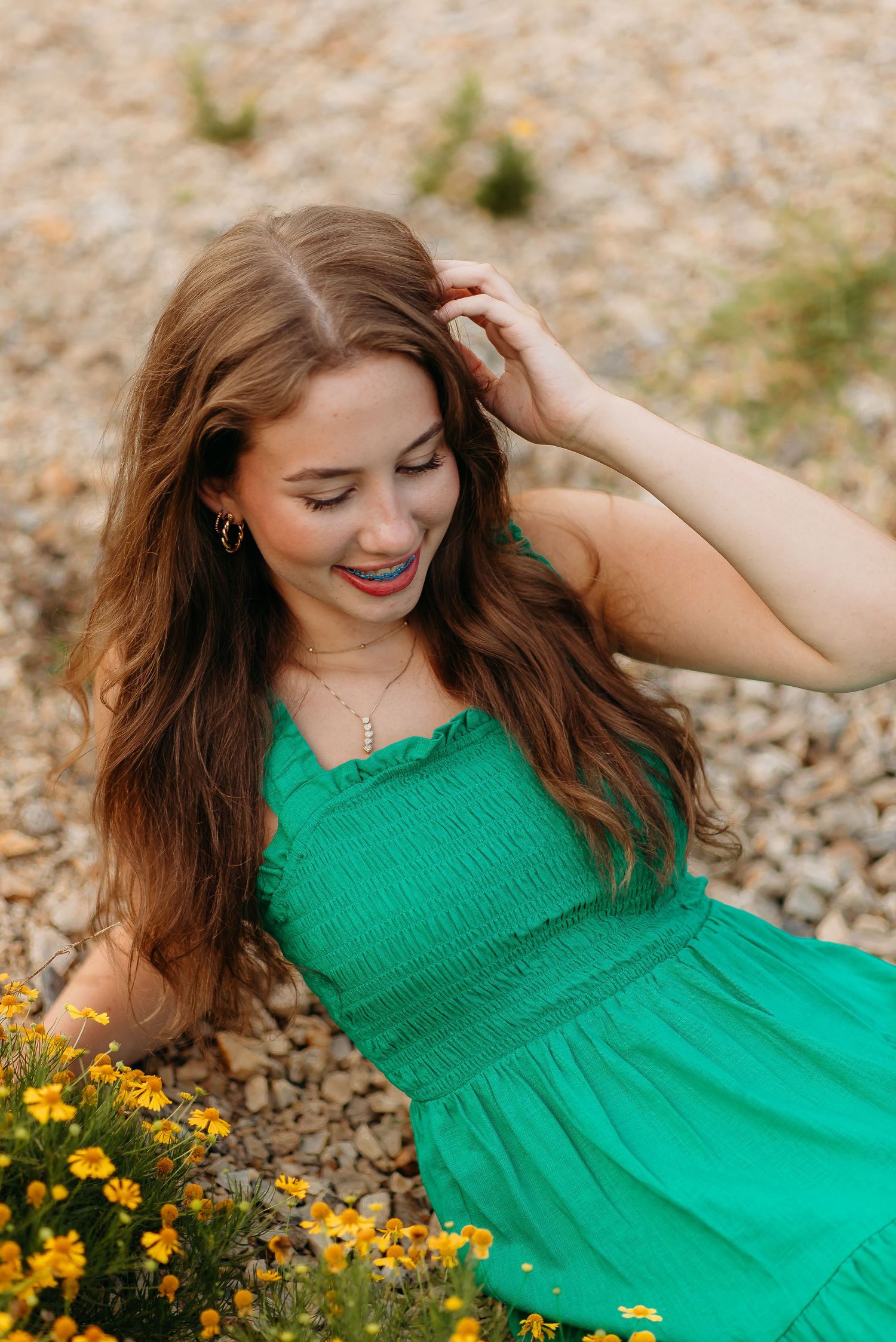A woman in a vibrant green sundress poses near yellow wildflowers during a summer photoshoot.