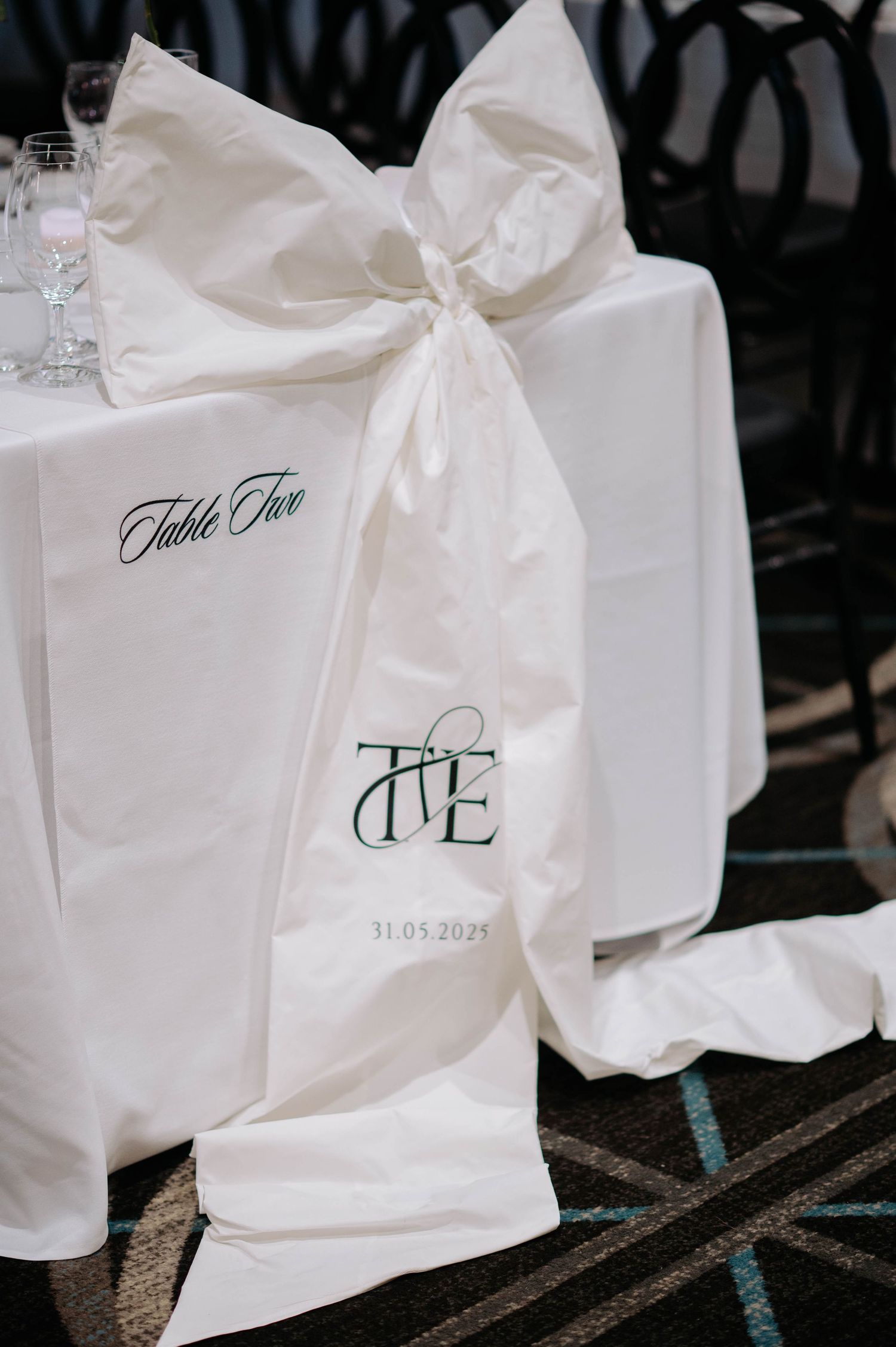 Elegant white wedding chair cover with table number and monogram decorations tied with a satin bow.